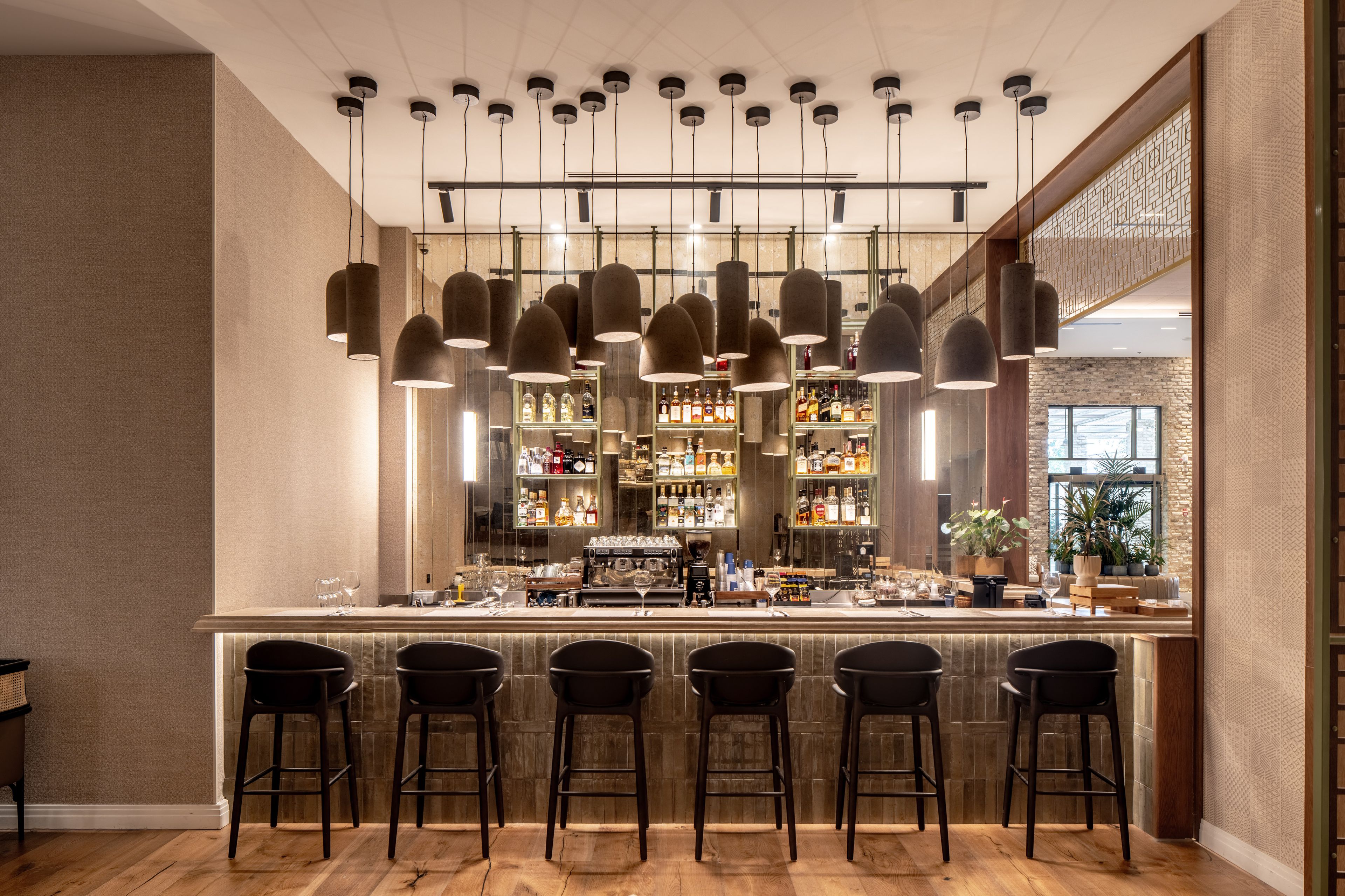A bar area with multiple hanging pendant lights, a bar counter with stools, and shelves stocked with bottles.
