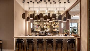 A bar area with multiple hanging pendant lights, a bar counter with stools, and shelves stocked with bottles.