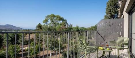Un balcon donnant sur un jardin et sur des collines lointaines.