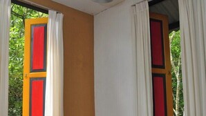 Una habitación con un banco, una mesa con una revista y dos ventanas con cortinas.