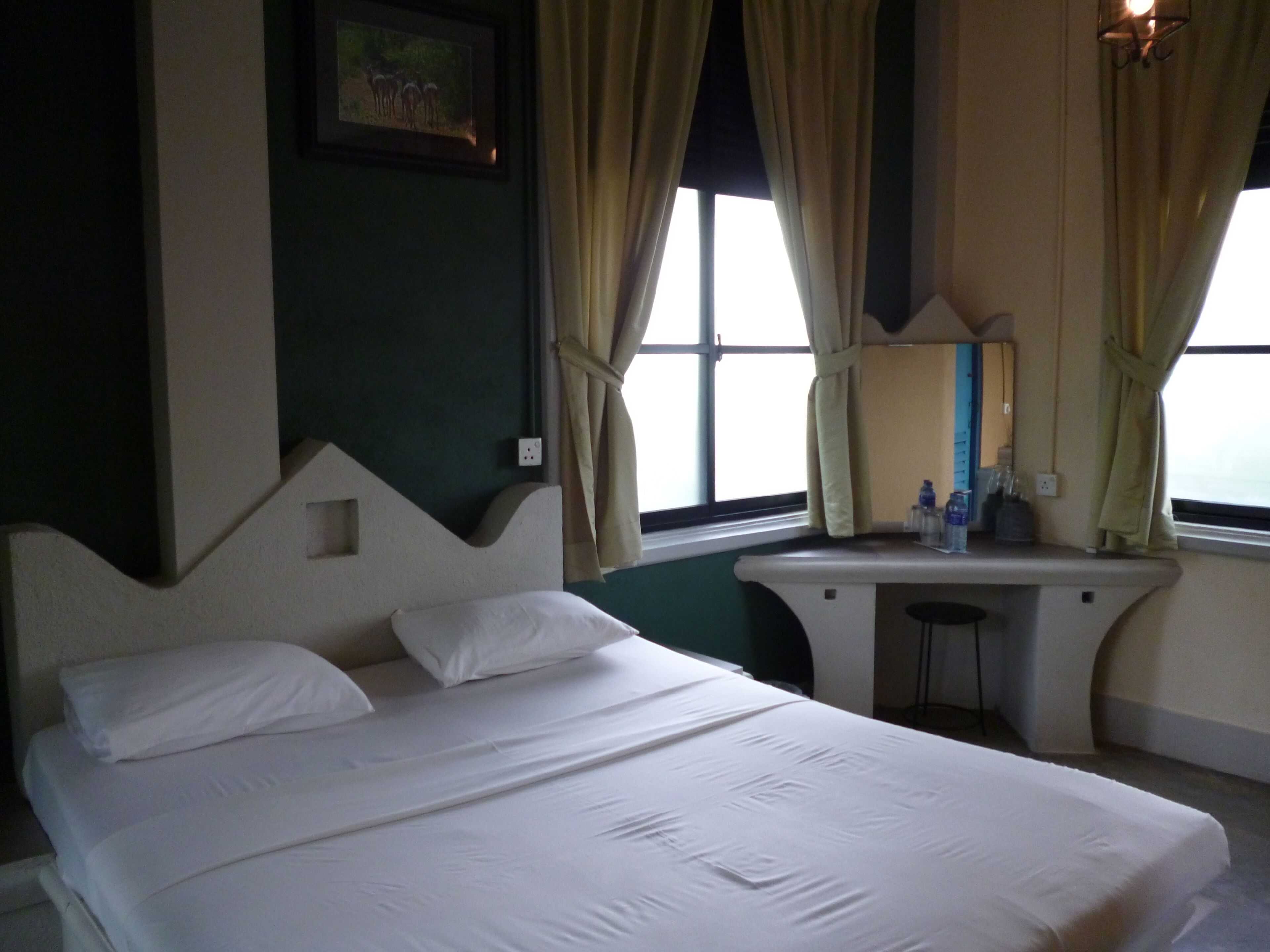 Een hotelkamer met een bed, een klein bureau, een spiegel en een raam met gordijnen.