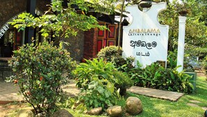 Un letrero que dice 'Ambalama Le Sure Lounge' con un jardín al frente.