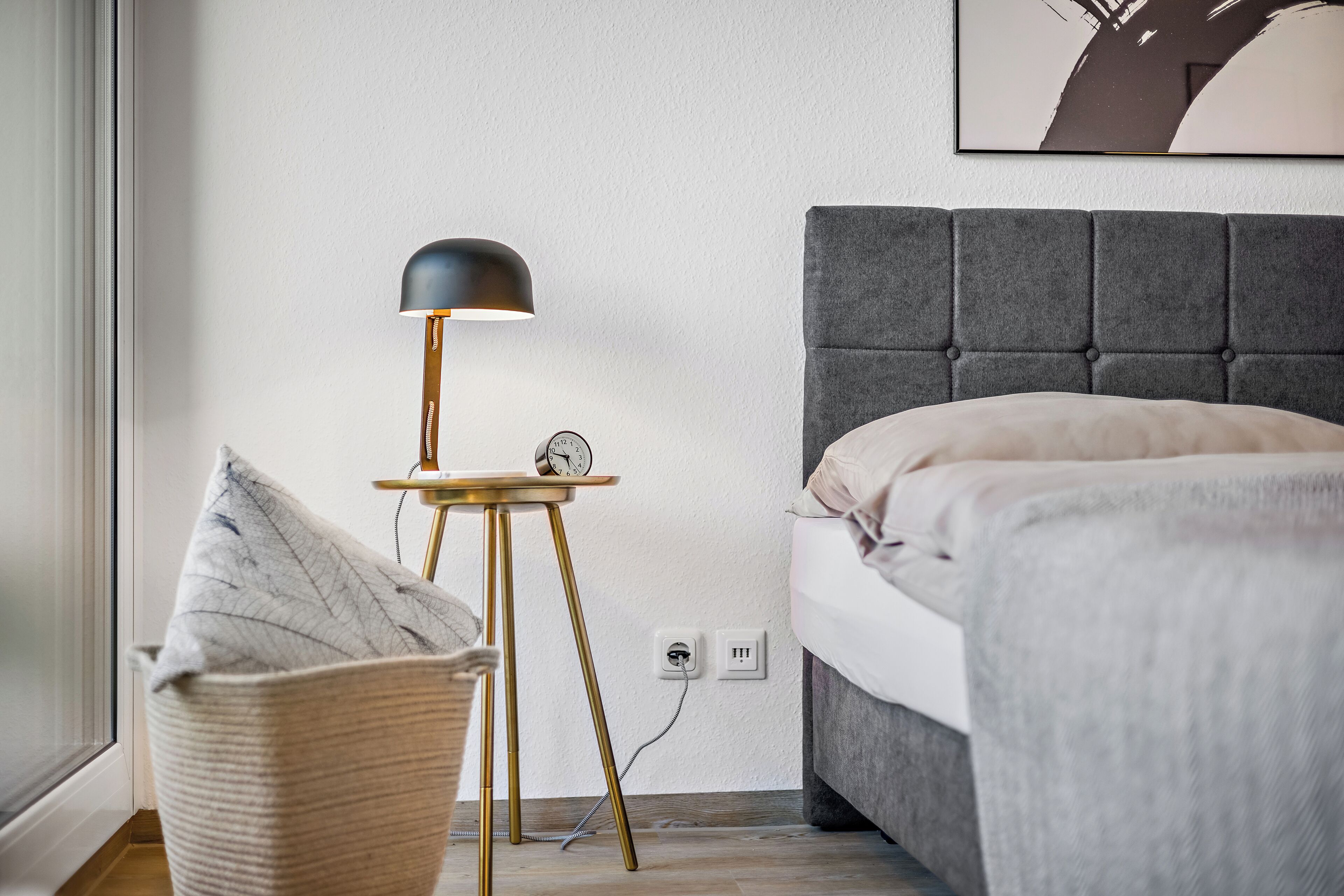 A bedroom with a bed, bedside table, lamp, and a clock.