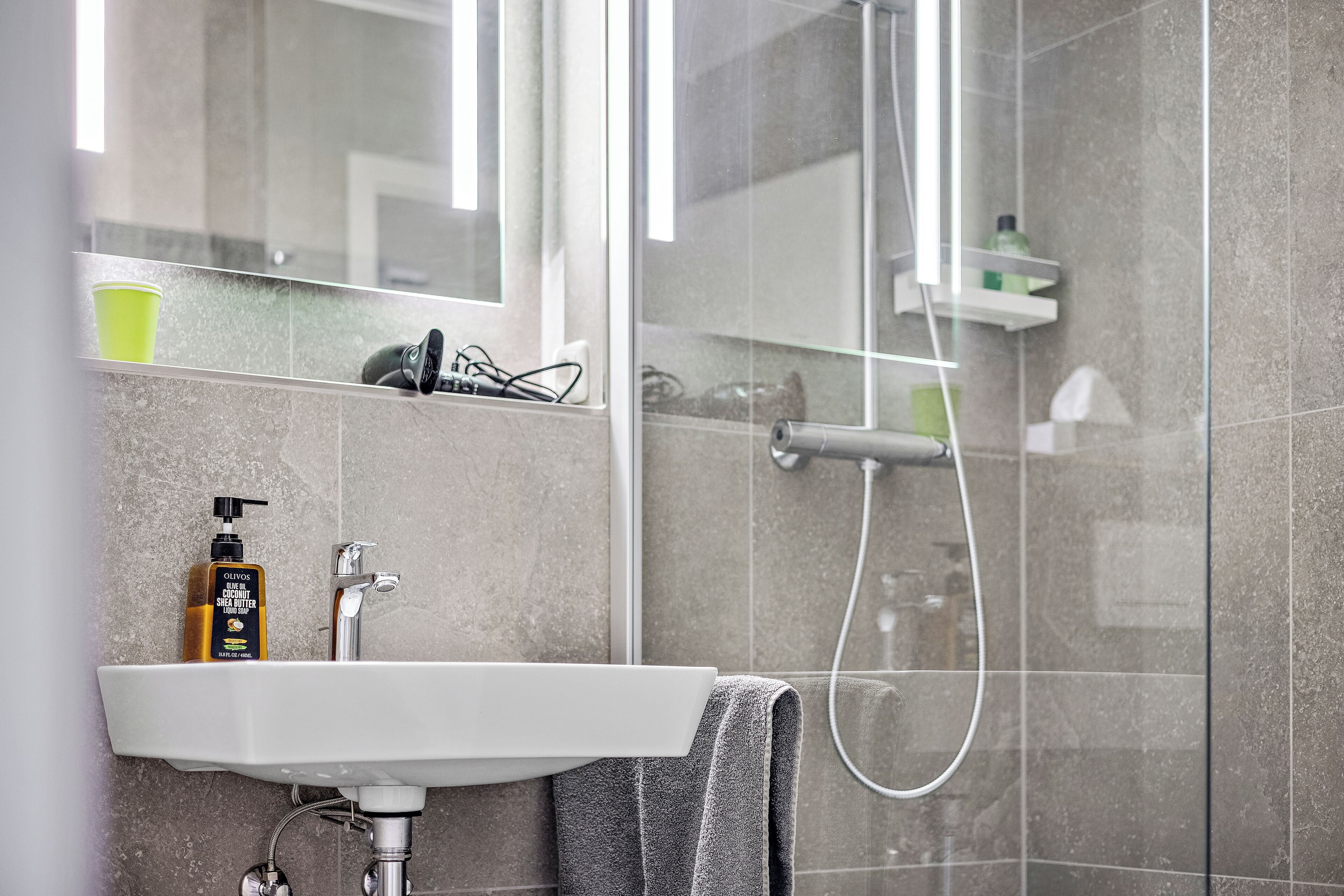 A modern bathroom with a white sink, a mirror, and a shower.