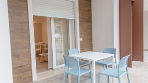 Une pièce moderne avec une table blanche et quatre chaises bleu clair, une porte-fenêtre coulissante et un mur d’accent en bois.