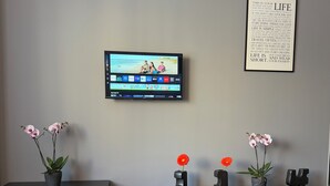A modern living room with a flat-screen TV mounted on the wall, a white abstract sculpture on a black table, and two black benches with potted plants.