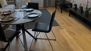 A modern hotel room with a dining area, a sofa, a TV, and potted plants.