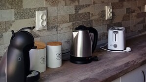 Una cocina con armarios blancos, salpicadero estampado, un hervidor, un tostador y dos recipientes para café.