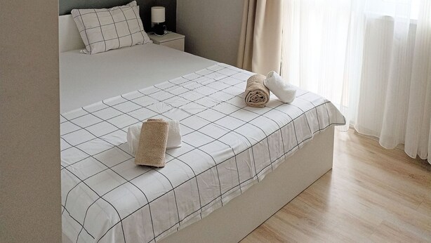 Una cama bien tendida con una colcha estampada, una mesita de noche con lámpara y una obra de arte abstracto en la pared.
