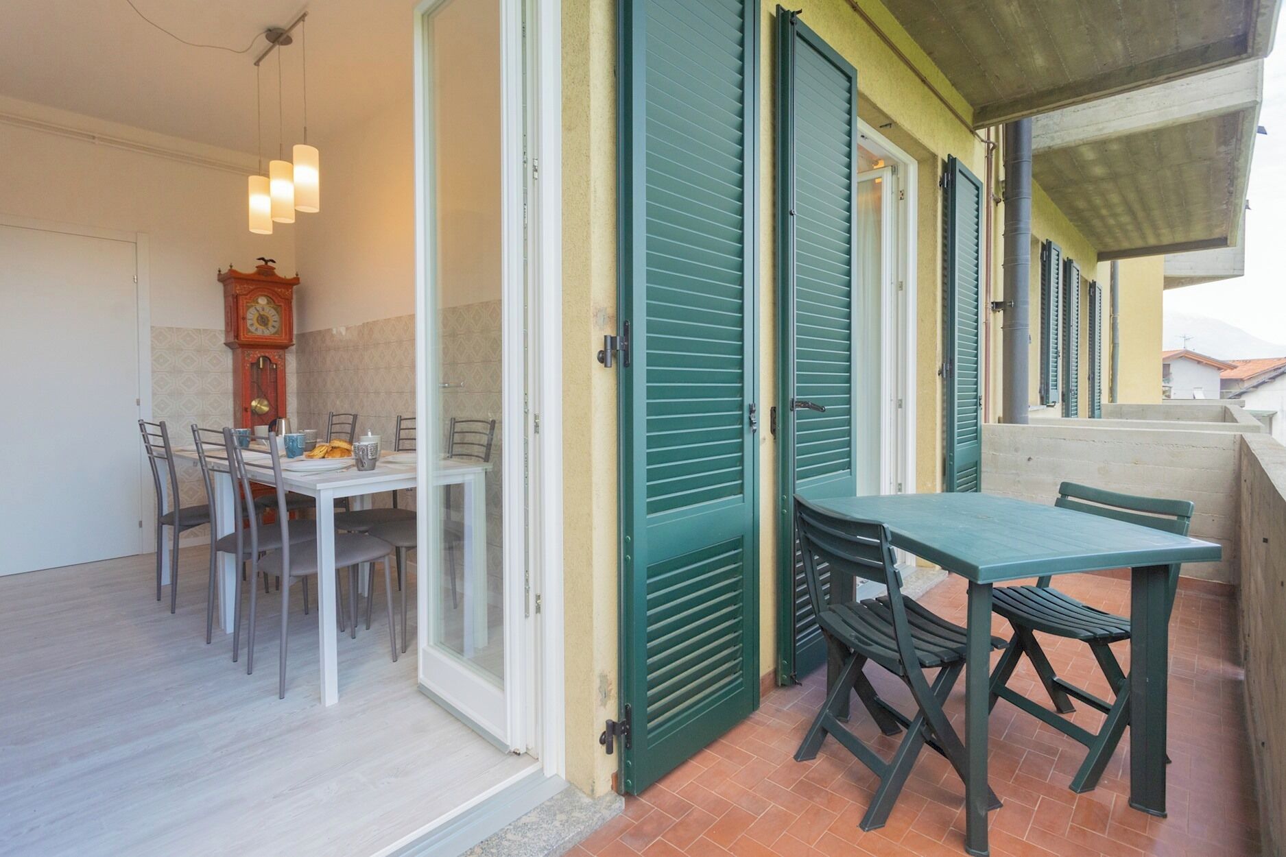 A dining area with a table and chairs, a clock, and green shutters on the windows.
