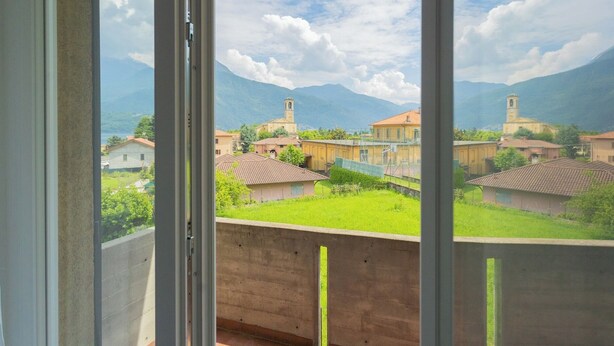 Ein Balkon mit Blick auf ein Dorf, darunter Häuser mit roten Dächern und eine Kirche mit Kirchturm.