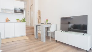 Eine moderne Küche mit weißen Schränken, einem Essbereich mit Tisch und Stühlen sowie einem Flachbildfernseher auf einem weißen Korpus.