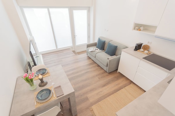 A modern kitchen with white cabinets, a dining table set with plates and a candle, and a sofa with cushions.