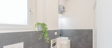 A modern bathroom with grey tiles, a white sink, a towel rack, and a window.