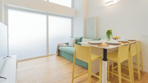 A bright living room with a large window, a sofa, a dining table with yellow chairs, and a white radiator. - A Step From the Lake Apartment by Rent all Como (Como)