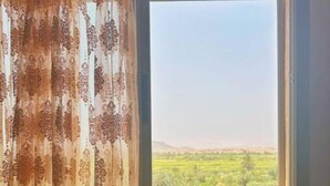 Una ventana con vistas a un paisaje verde, una cortina con estampado floral y un cojín con diseño floral.
