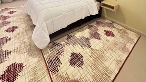 Un dormitorio con cama, mesita de noche, espejo en la pared y ventana con cortinas.