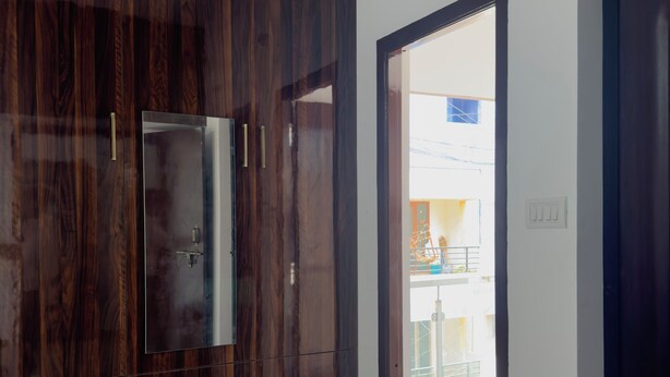 A room with a dark wood wardrobe, a door leading to an outdoor balcony, and a tiled floor. - Sishya Service Apartment - Chennai OMR  (Chennai)