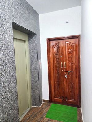 Un pasillo con una pared gris con textura, una puerta verde y un par de puertas de madera con intrincados grabados.