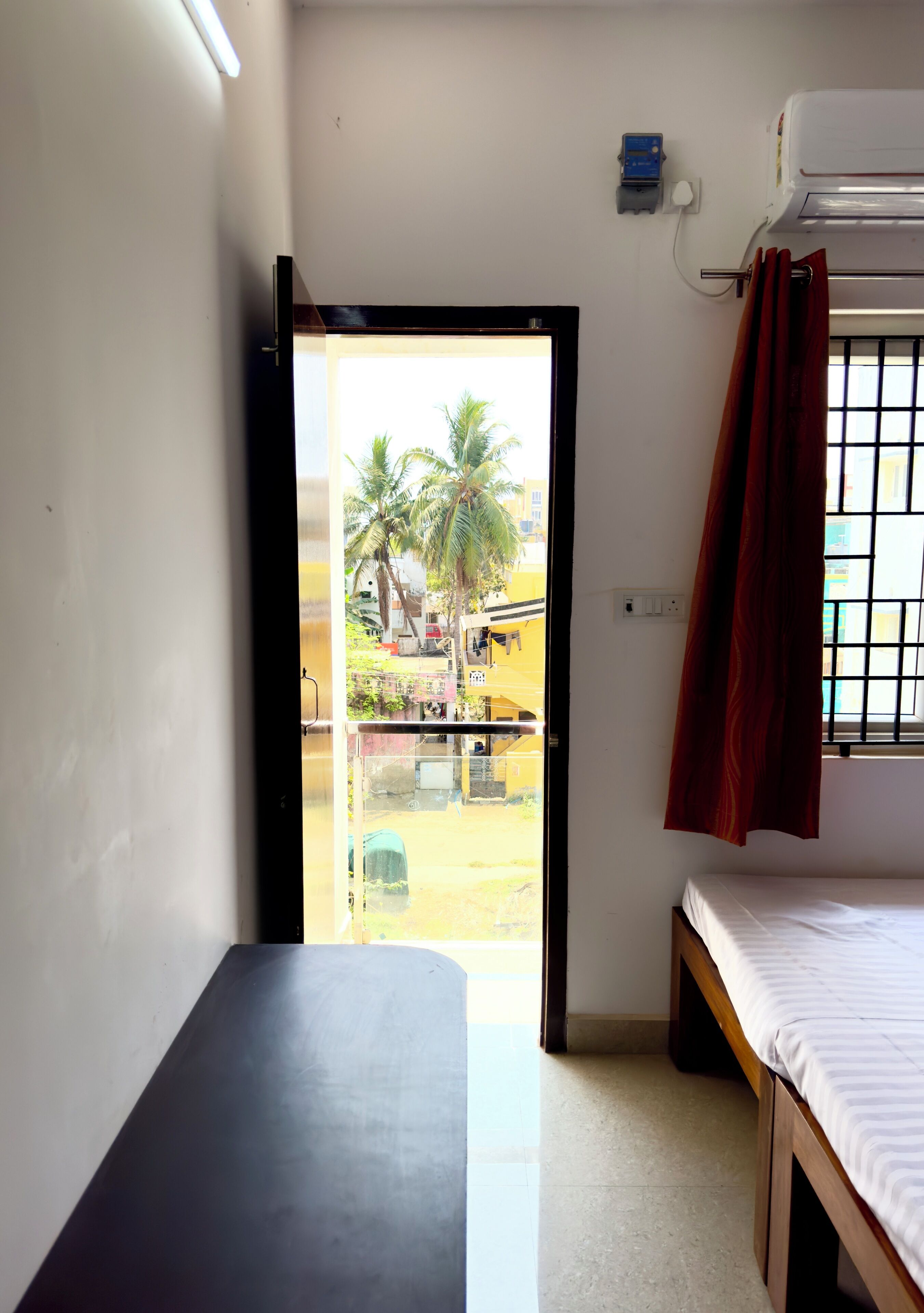A room with a bed, a small table, a window with a curtain, and an air conditioning unit.
