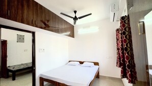 A bedroom with a bed, wooden wardrobe, ceiling fan, and a bathroom with a shower curtain. - Sishya Service Apartment - Chennai OMR  (Chennai)