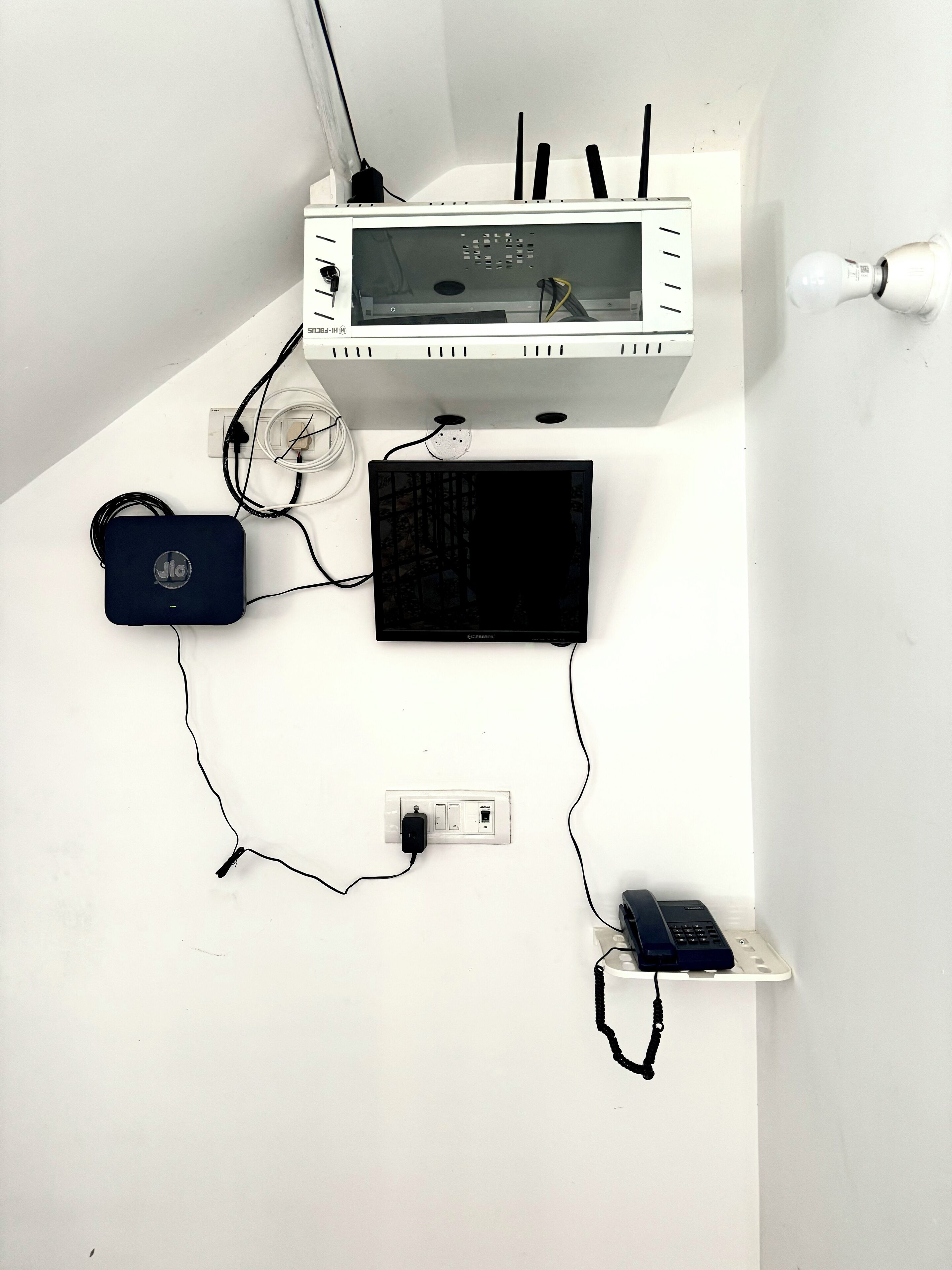 Eine weiße Wand mit einem weißen Stromkasten, einem schwarzen Gerät und einem blauen Gerät, die/das damit verbunden ist.