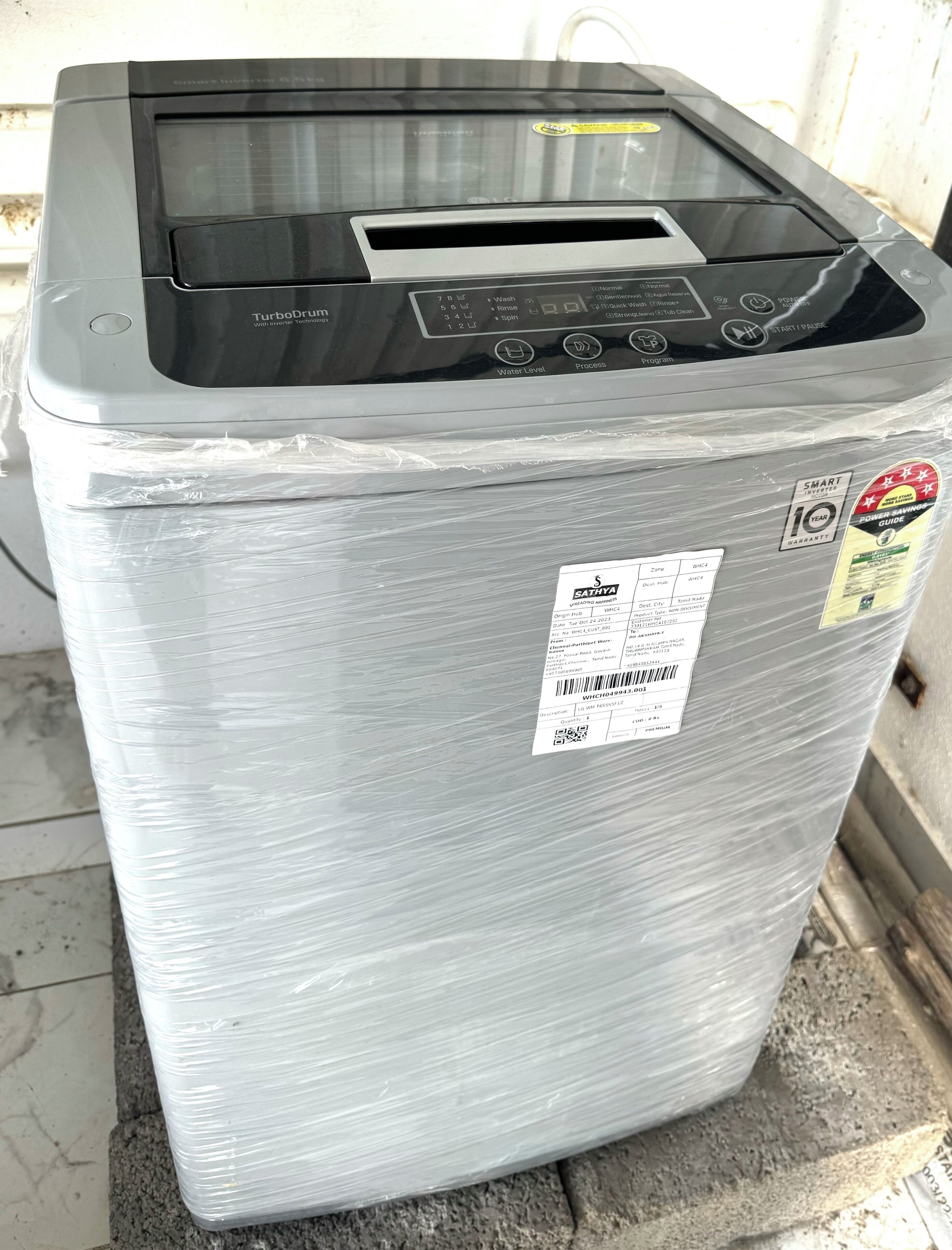 A white, compact washer-dryer unit with a digital control panel, wrapped in plastic.