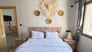 A bedroom with a large bed, a wooden headboard, a wall-mounted decorative item, and a window with curtains.