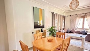 A dining area with a wooden table and chairs, a potted plant, and a sofa with cushions.