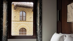 A hotel room with a bed, a window with a view of a brick building, and a marble wall. - Palazzo Ottaviani Luxury Apartments (Florence)