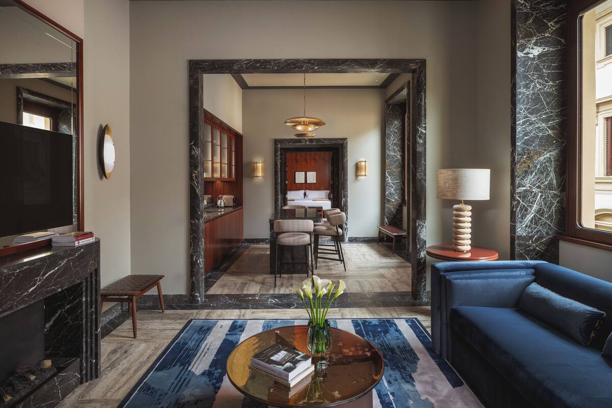 Un moderno vestíbulo de hotel con un sofá azul, una mesita de centro con libros, un televisor y una chimenea.