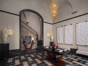 A lobby with a marble floor, a staircase, a round table with books, and wall art. - Palazzo Ottaviani Luxury Apartments (Florence)