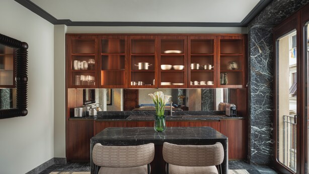 A kitchen with dark wood cabinets, a marble countertop, and two wicker chairs. - Palazzo Ottaviani Luxury Apartments (Florence)