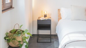 Un dormitorio con cama, mesita de noche, lámpara y planta en maceta.