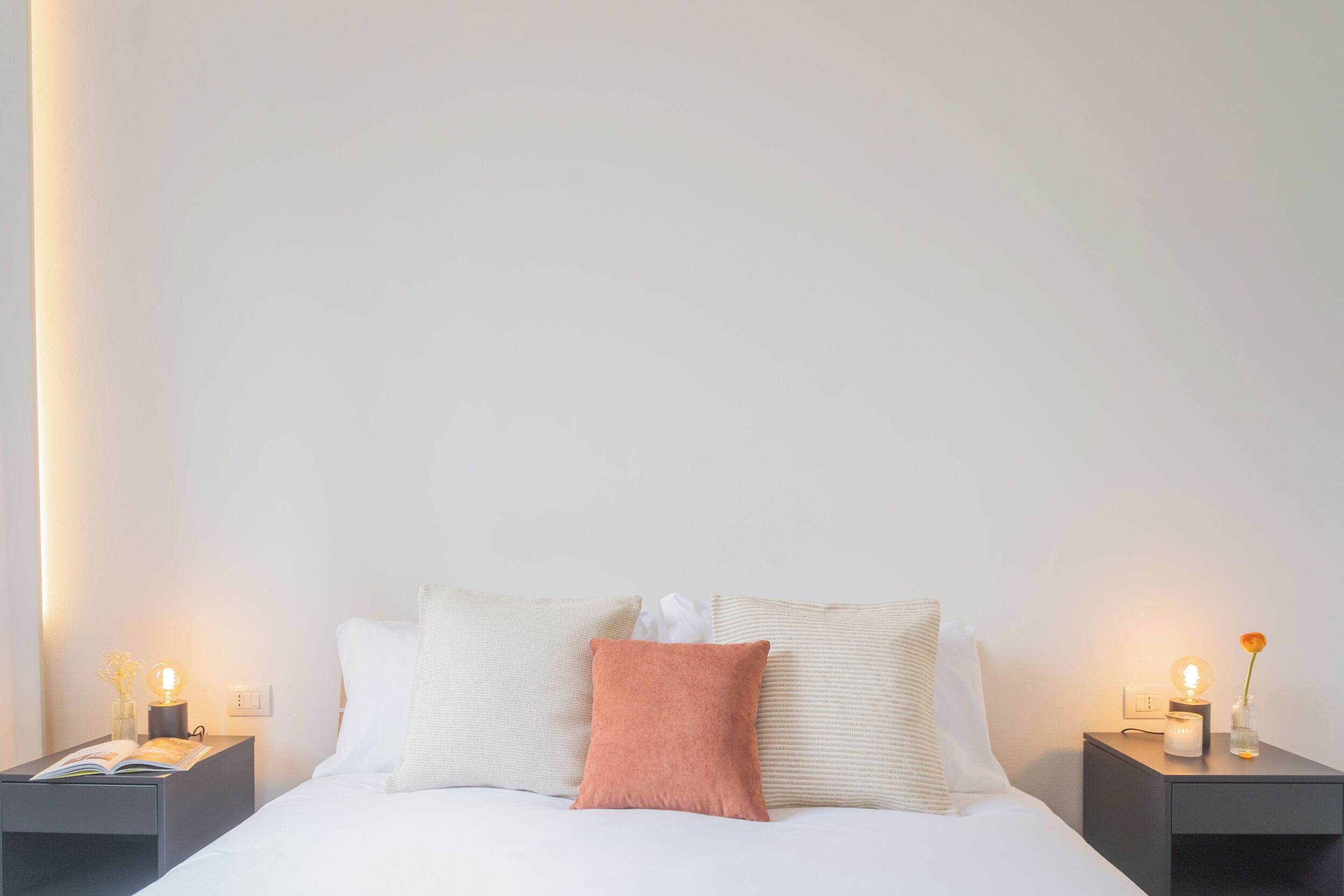 Una cama bien hecha con almohadas y un libro sobre una mesita de noche.