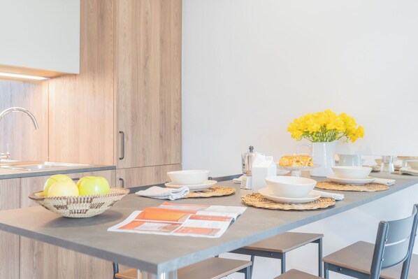Une cuisine moderne avec des meubles en bois, un îlot central sur lequel se trouve un saladier rempli de citrons, un vase de fleurs jaunes et un journal ouvert.