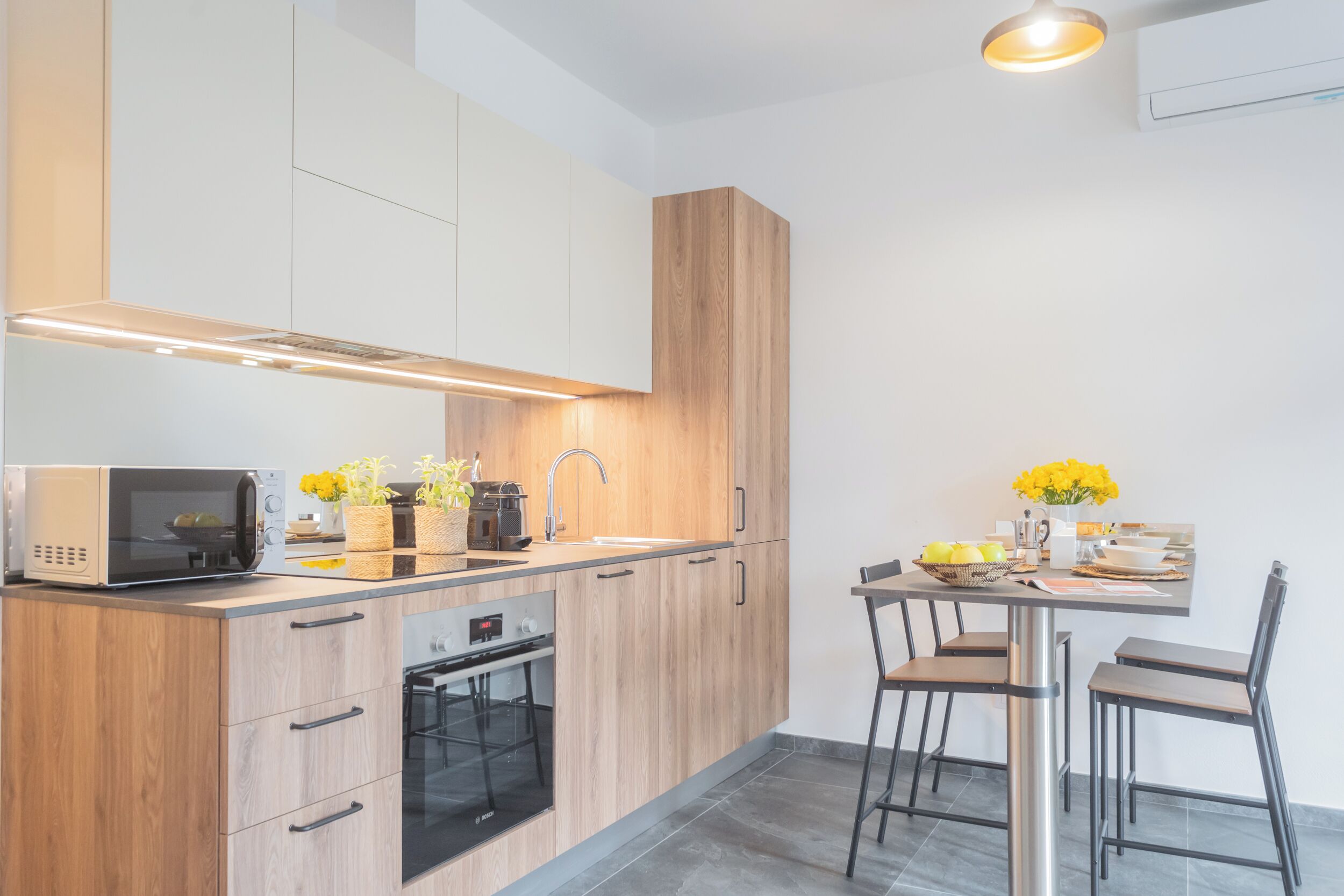 A modern kitchen with wooden cabinets, a built-in oven, and a dining area with a table and chairs.