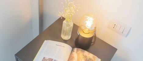 A neatly arranged bedside table with a book, a vase with flowers, and a lamp.