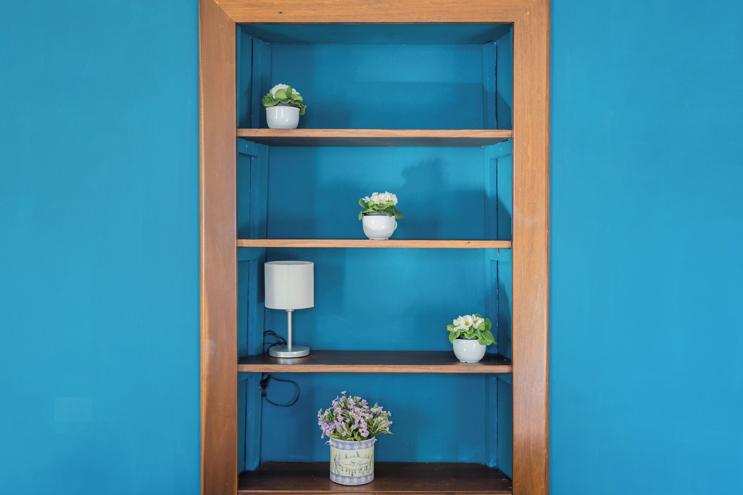 Une étagère en bois, composée de trois étagères, est adossée à un mur bleu.