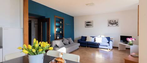 A modern living room with a blue accent wall, a grey sofa, and a dining area with a table and chairs.