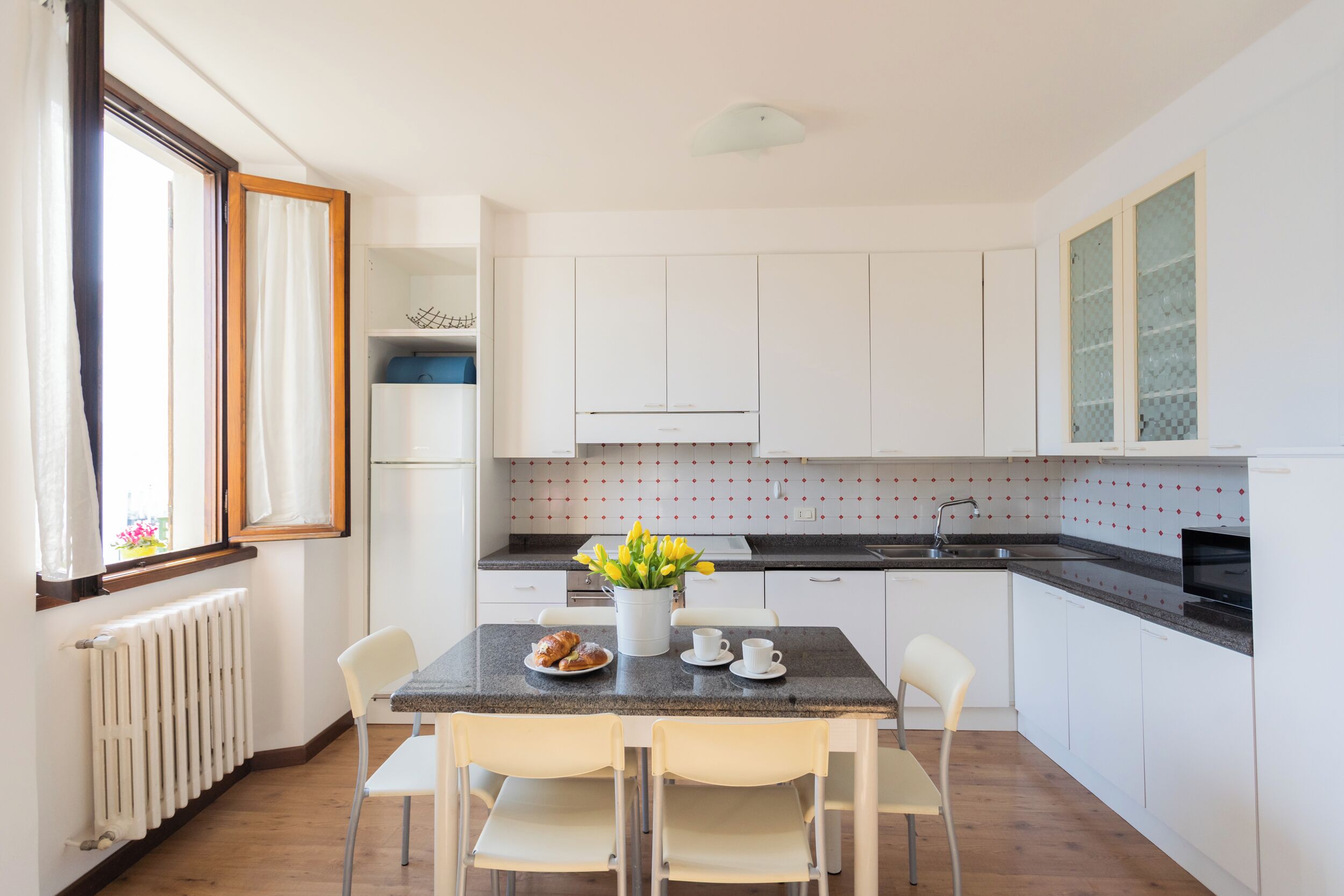 Una cucina moderna con mobili bianchi, un piano di lavoro in granito e un'area pranzo con due sedie e un tavolo.