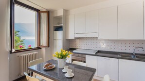 A modern kitchen with white cabinets, a granite countertop, and a view of the sea through a window. - Family Lake Apartment by Rent all Como (Tremezzina)