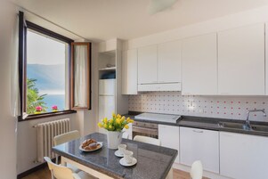 Una cucina moderna con mobili bianchi, un piano di lavoro in granito e vista sul mare attraverso una finestra.