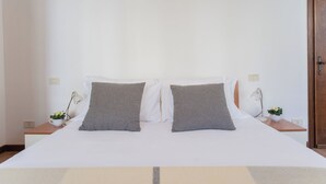 A neatly made bed with white and gray bedding, two bedside tables with lamps and small potted plants, and a wooden door on the right. - Family Lake Apartment by Rent all Como (Tremezzina)