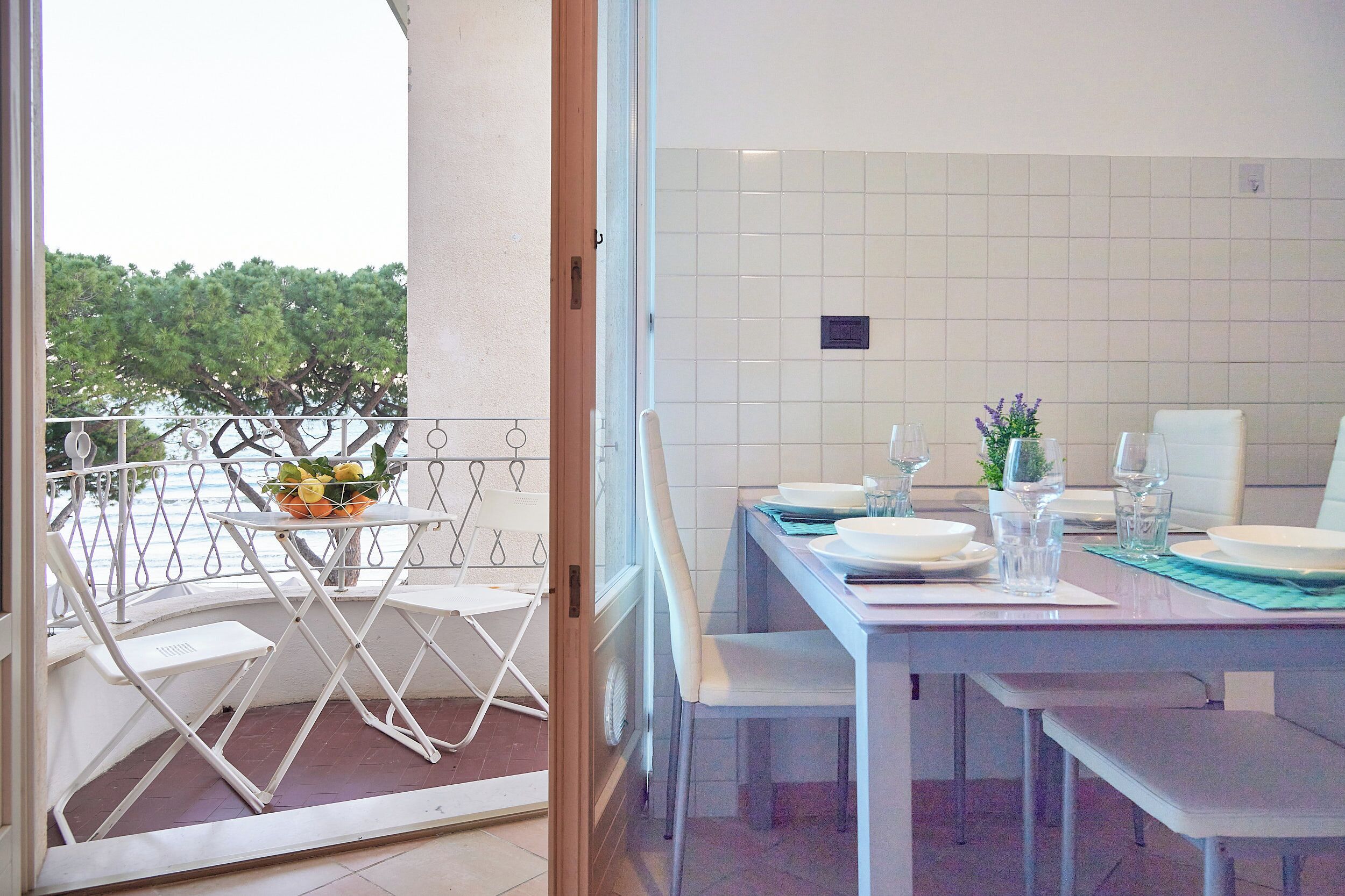 Un balcón con mesa lista para comer, sillas y una pequeña mesa con un cuenco de fruta.