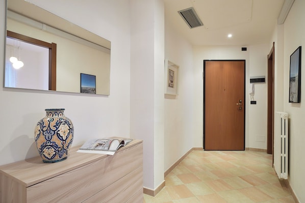 Un couloir avec une porte en bois, un radiateur et un vase posé sur une commode.