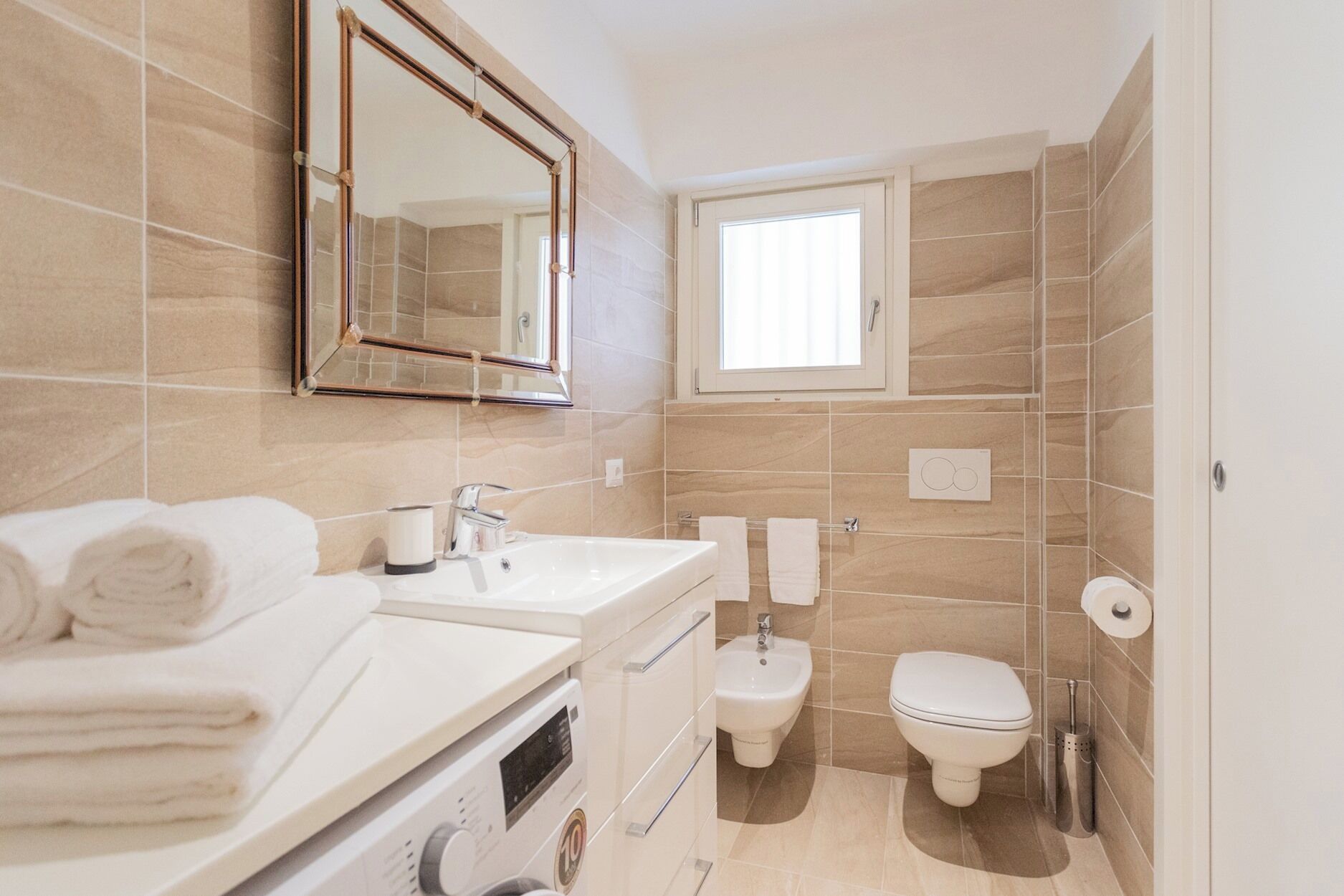 A modern bathroom with a large mirror, two sinks, a toilet, and a bidet.