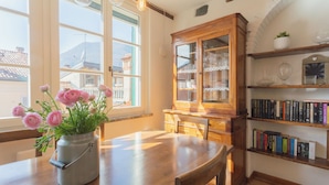 Un comedor con una mesa de madera, un jarrón de flores rosas y una estantería con libros.