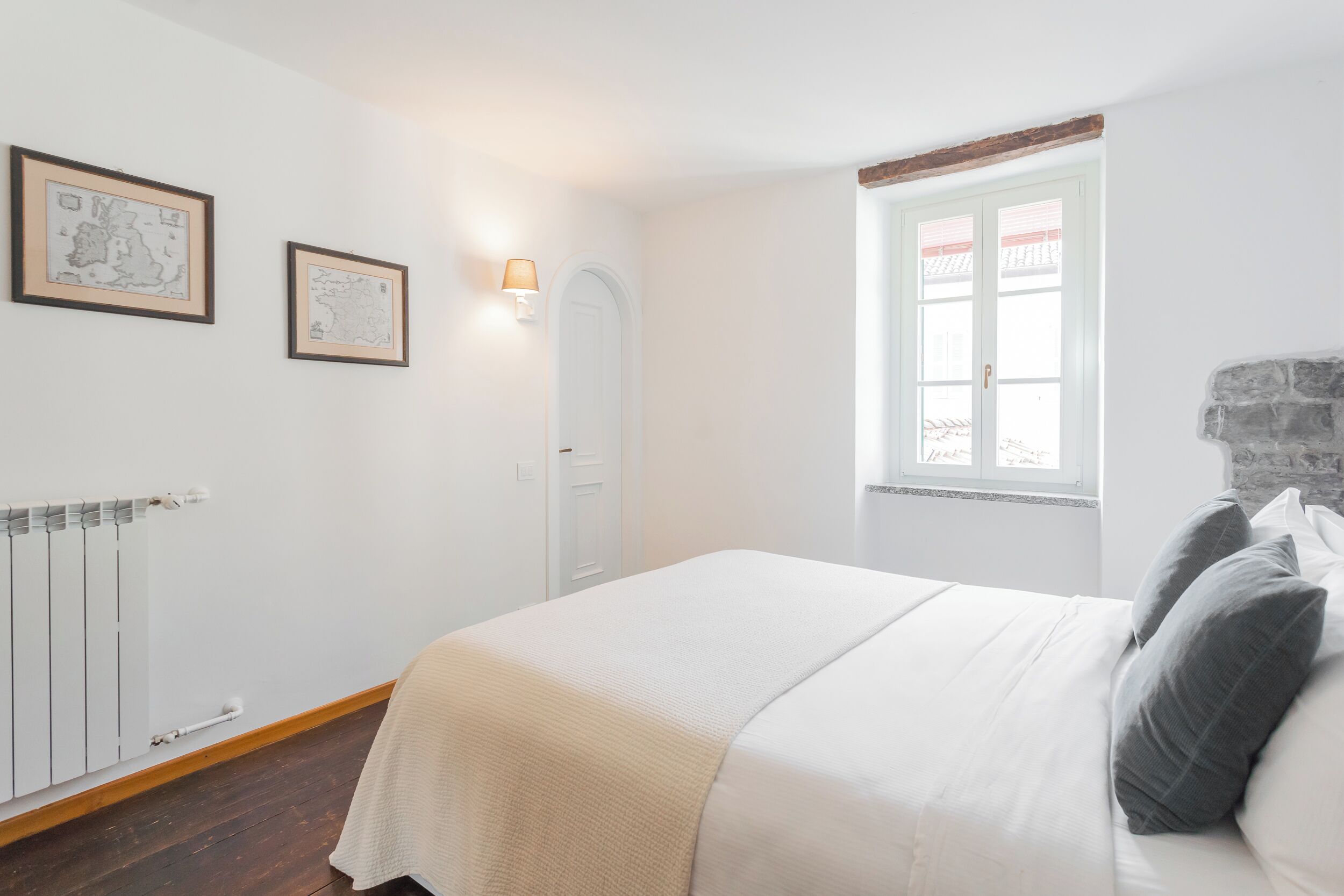 Een slaapkamer met een bed, een radiator, een raam met uitzicht en twee ingelijste foto's aan de muur.