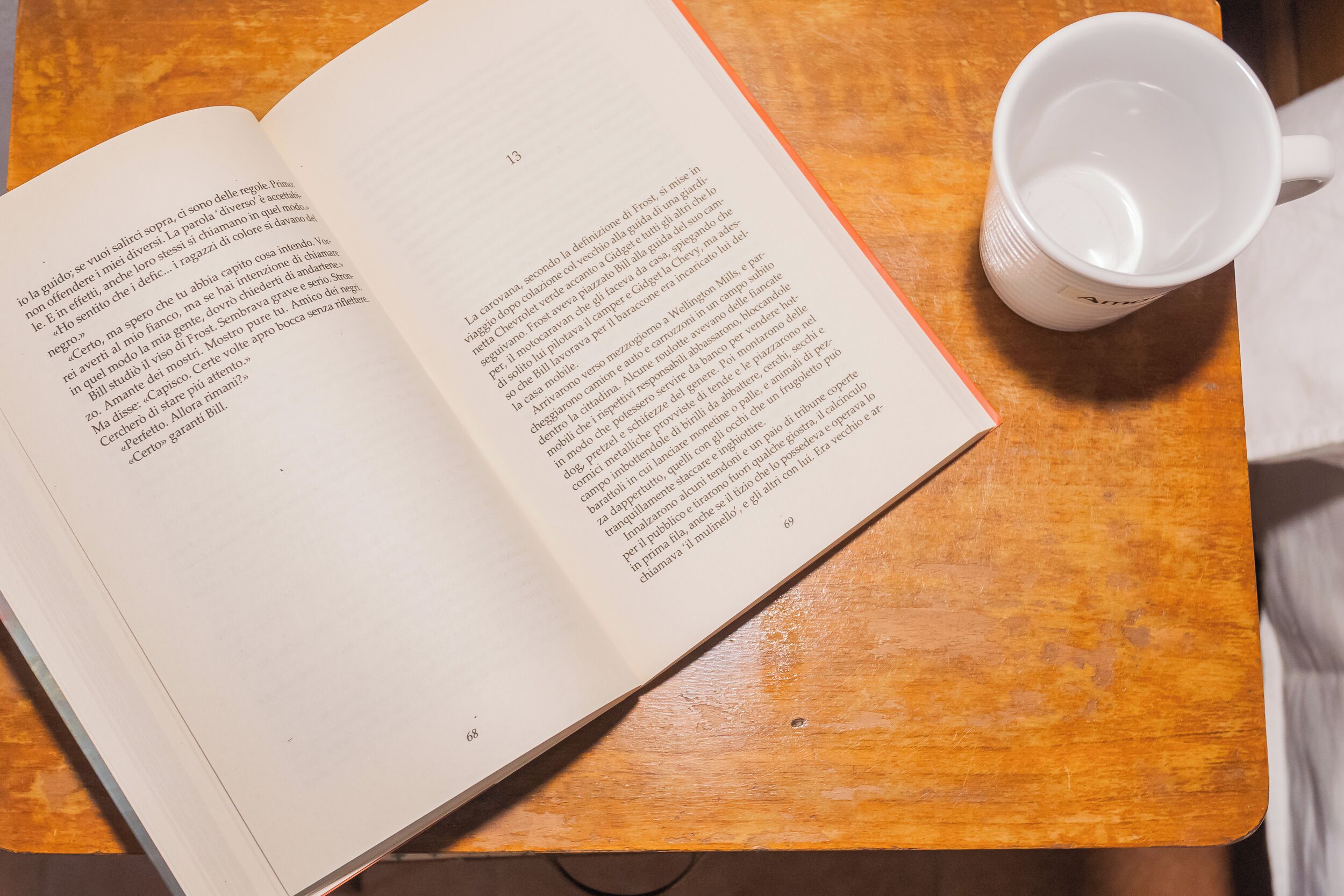 Een open boek op een houten tafel, met een witte mok ernaast.